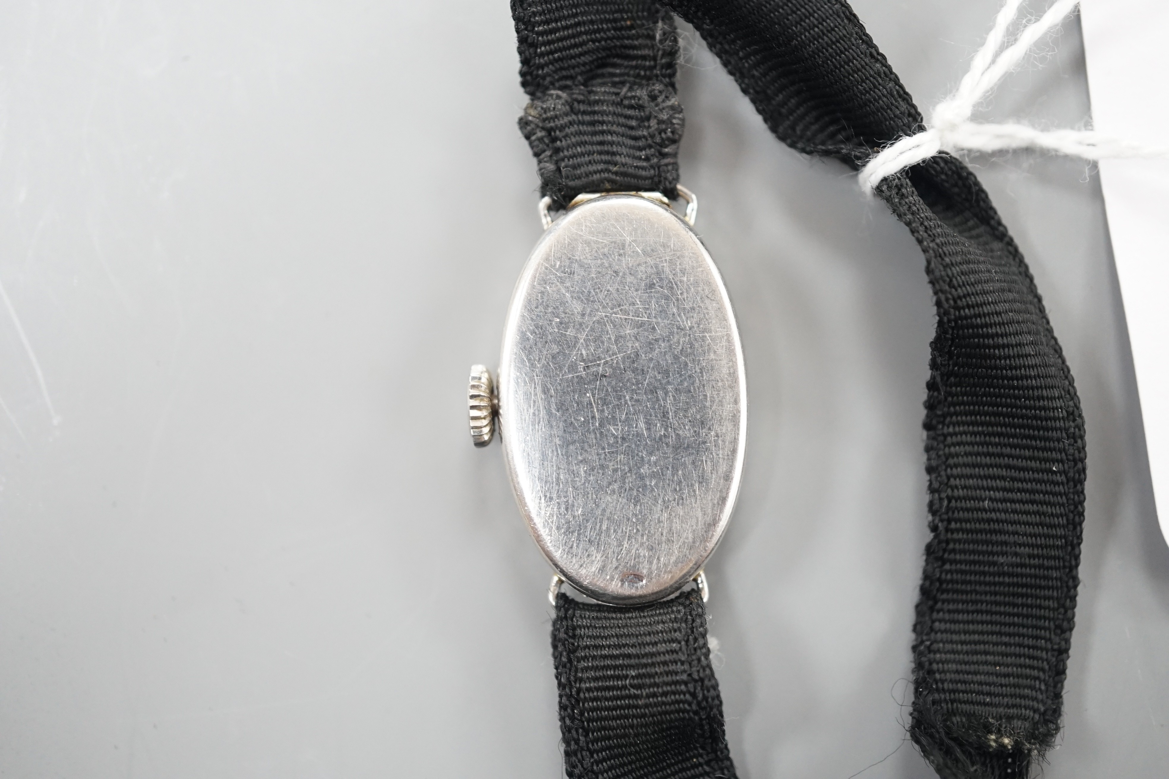 A lady's white metal (stamped platine) and diamond set oval cocktail watch, on a black sash bracelet, gross weight 13.9 grams.